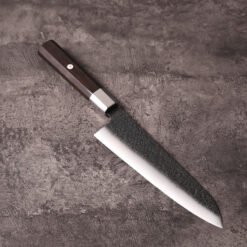AUS-10 gyuto knife angled on stone with kurouchi finish and reverse-tanto tip