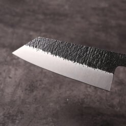 Close-up of K-Bunka blade showing kurouchi forge scale above hand-ground mirror bevel