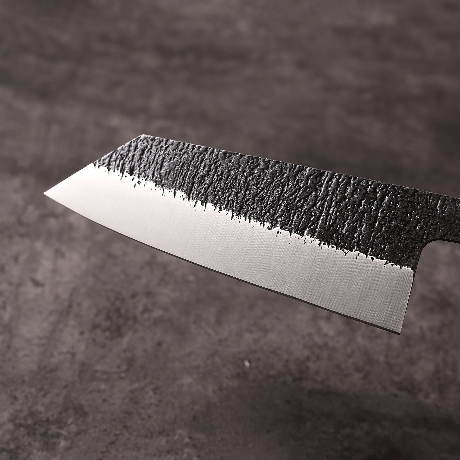 Close-up of K-Bunka blade showing kurouchi forge scale above hand-ground mirror bevel