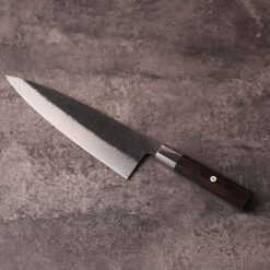 Japanese-style 240mm gyuto knife with black textured blade on stone surface