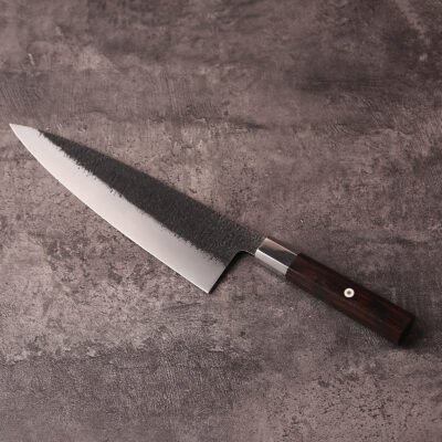 Japanese-style 240mm gyuto knife with black textured blade on stone surface